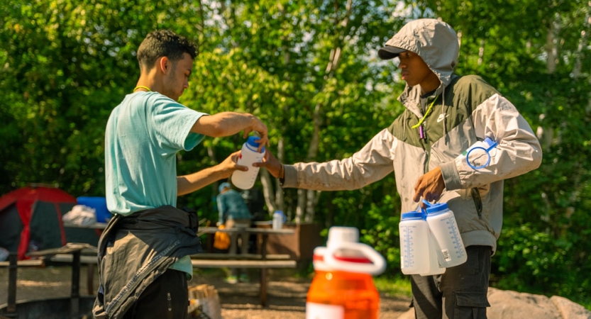 One person hands a water bottle to another while outdoors